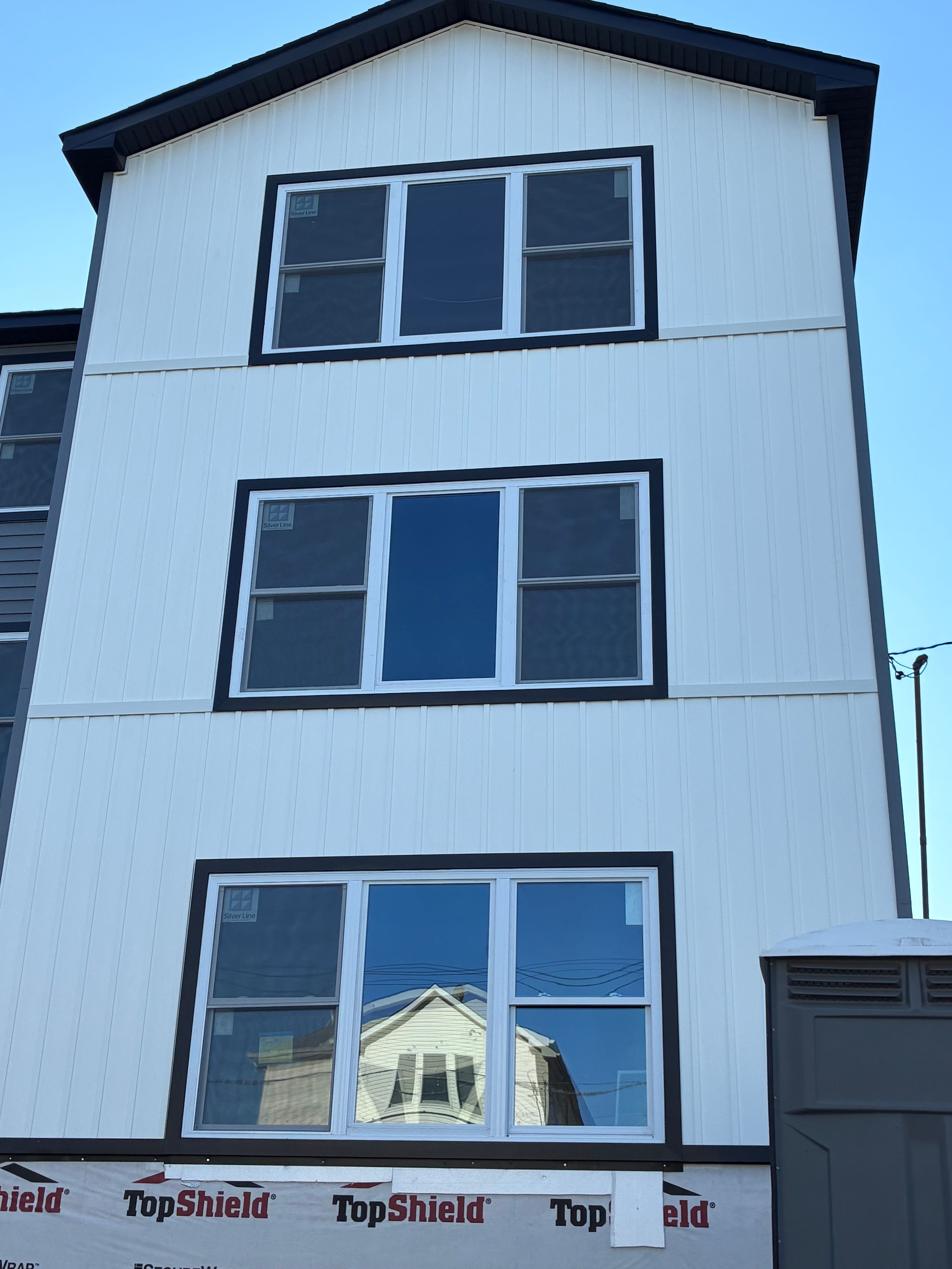 Three-storey new build with fresh white vertical siding and black window trim — NYE General Construction