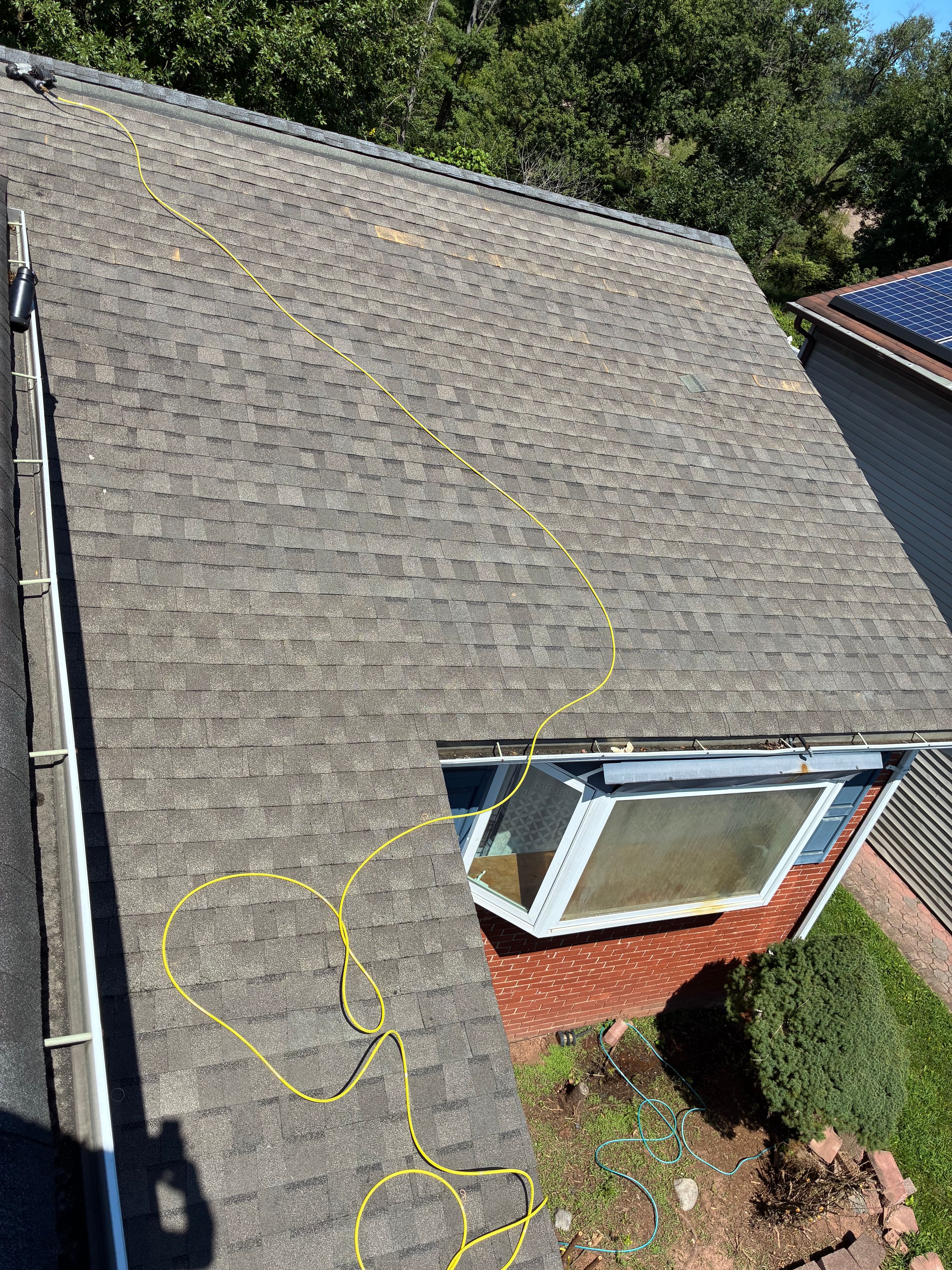 Steep shingle roof slope over a bay window during a roofing job, gutter run at the eave — NYE General Construction