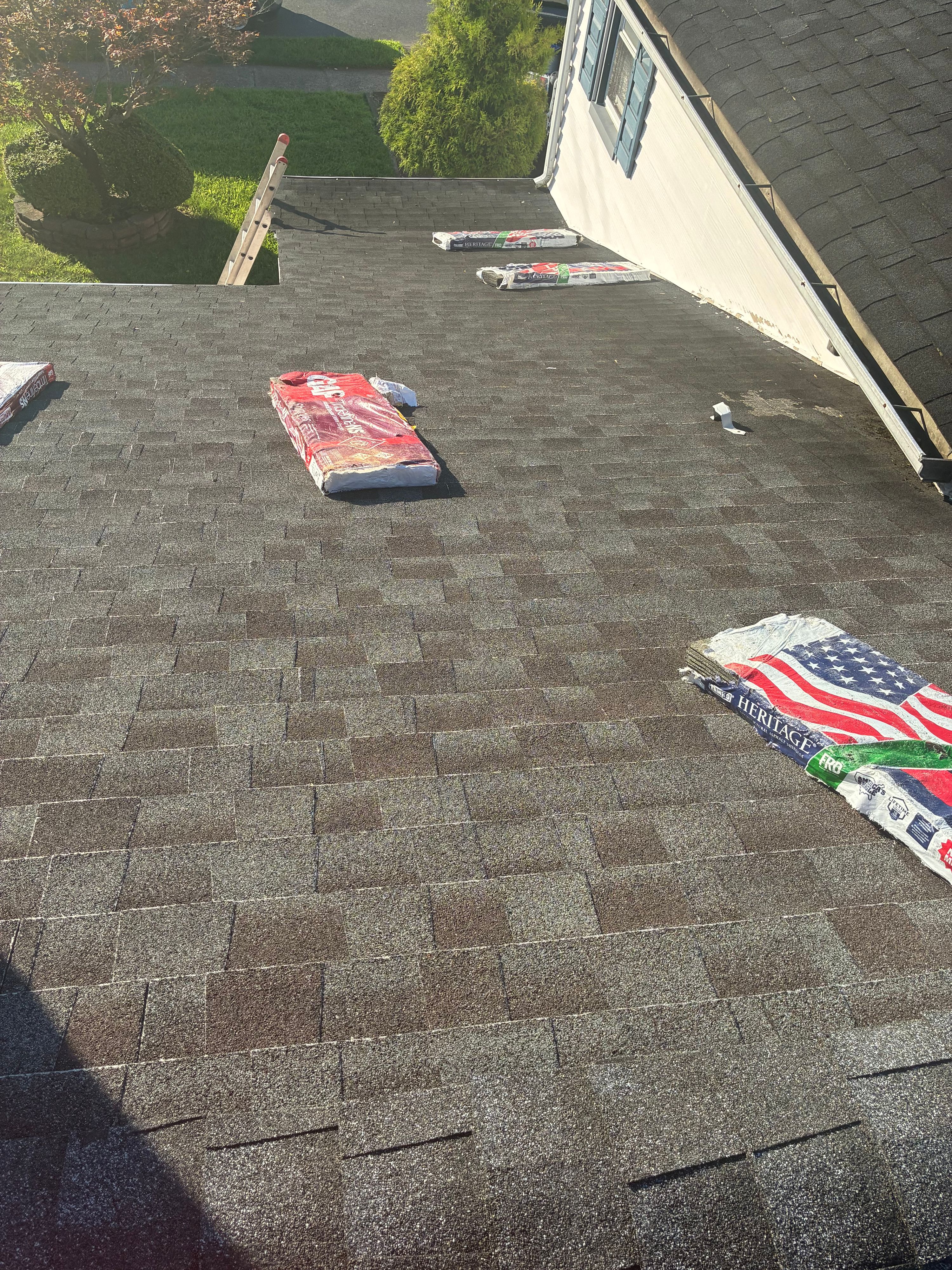 New architectural shingles installed with bundles staged on the roof and a ladder at the eave — NYE General Construction