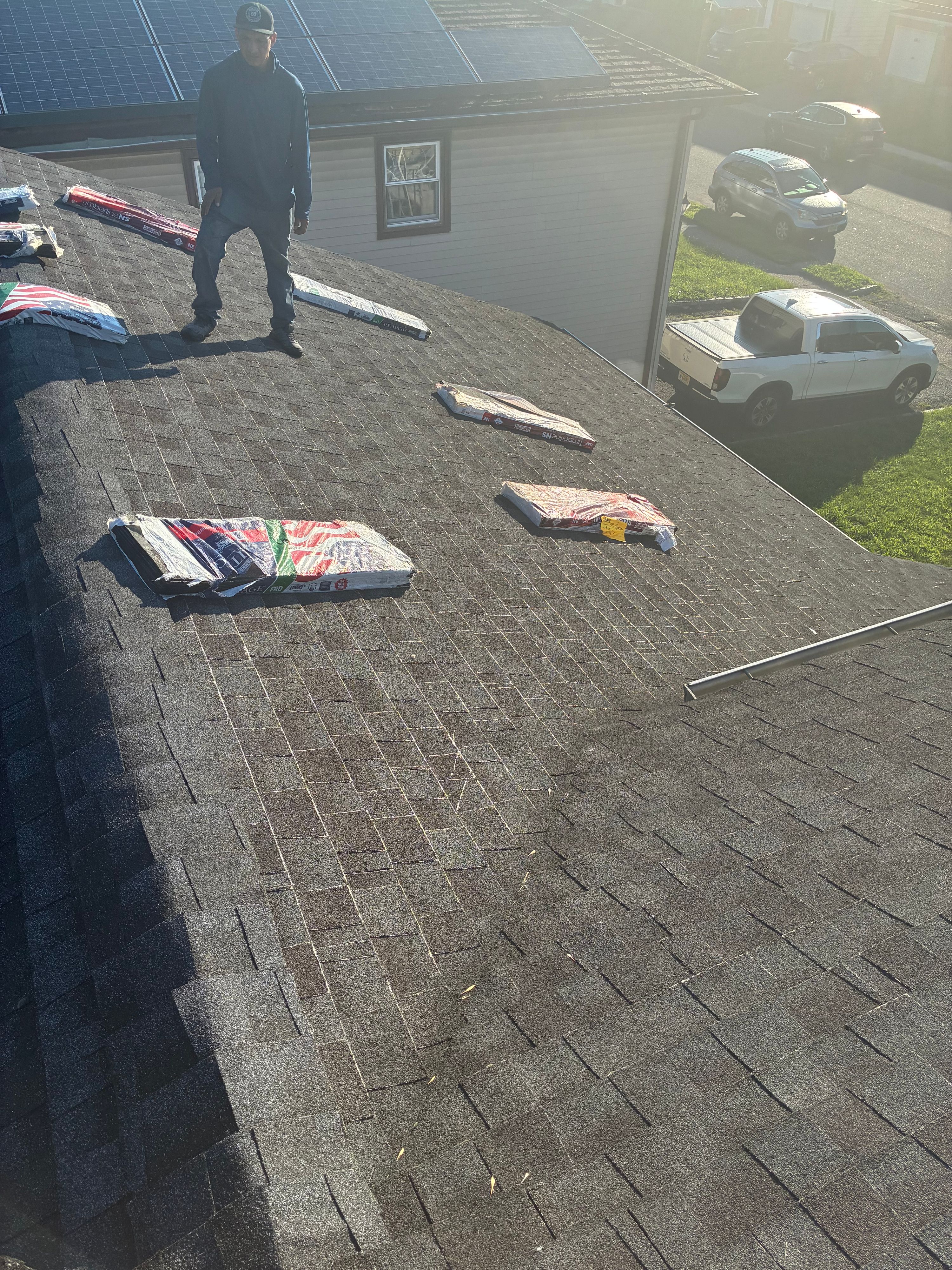 Crew member laying architectural shingles on a residential roof, bundles staged along the slope — NYE General Construction