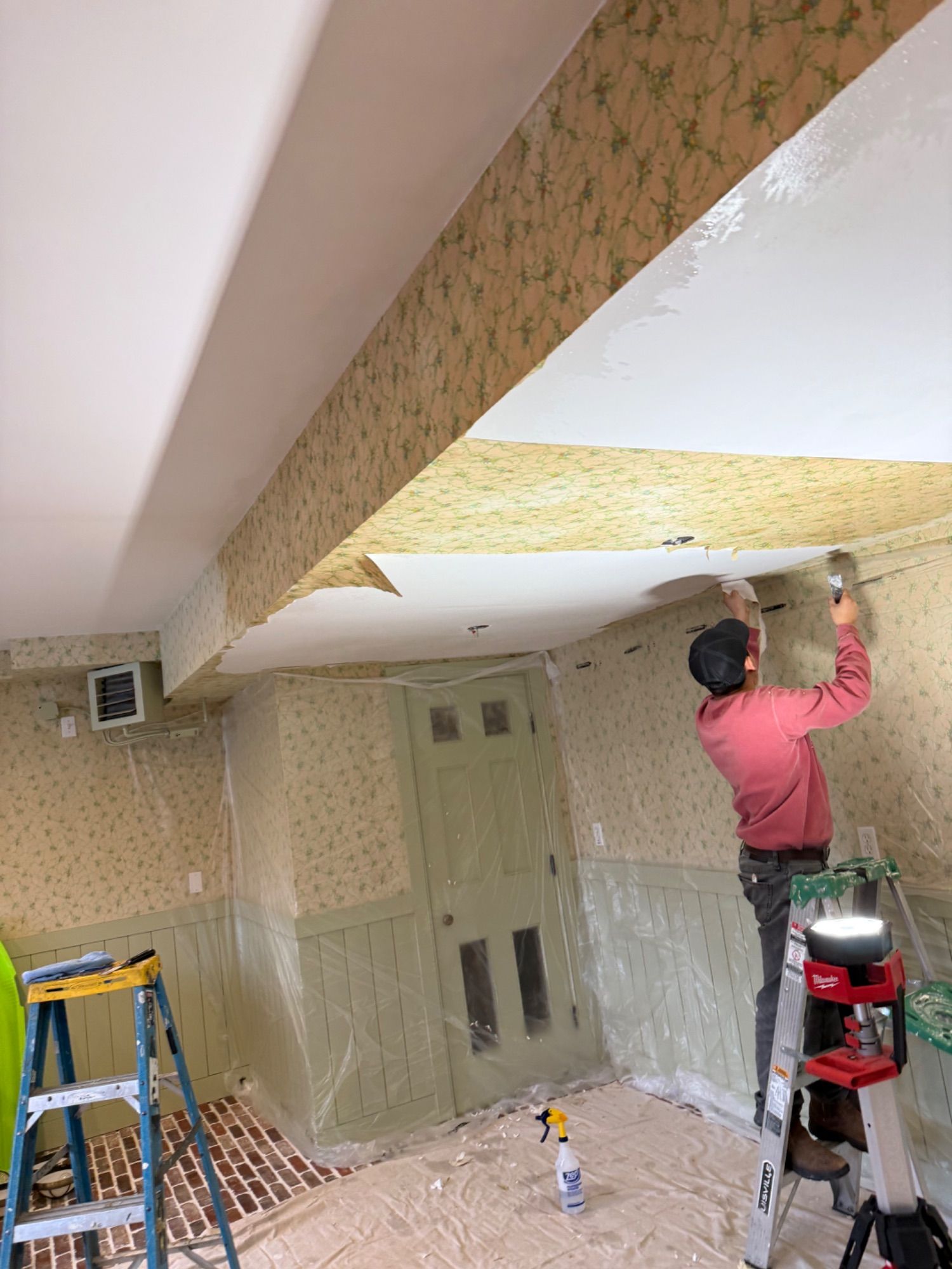 A Soto Painting Corporation painter on a ladder stripping a wallpapered ceiling before repainting