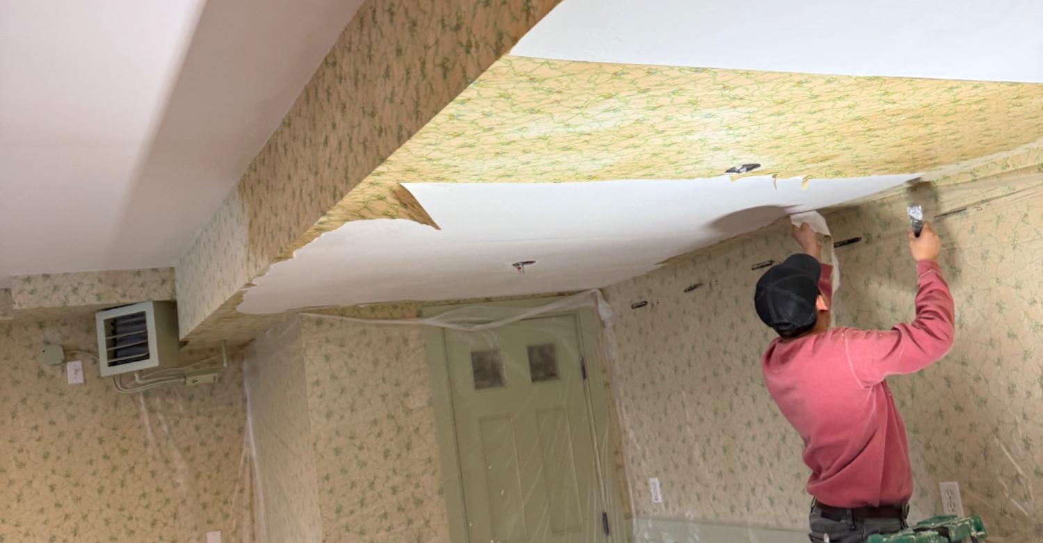 A Soto Painting Corporation painter on a ladder stripping a wallpapered ceiling before repainting