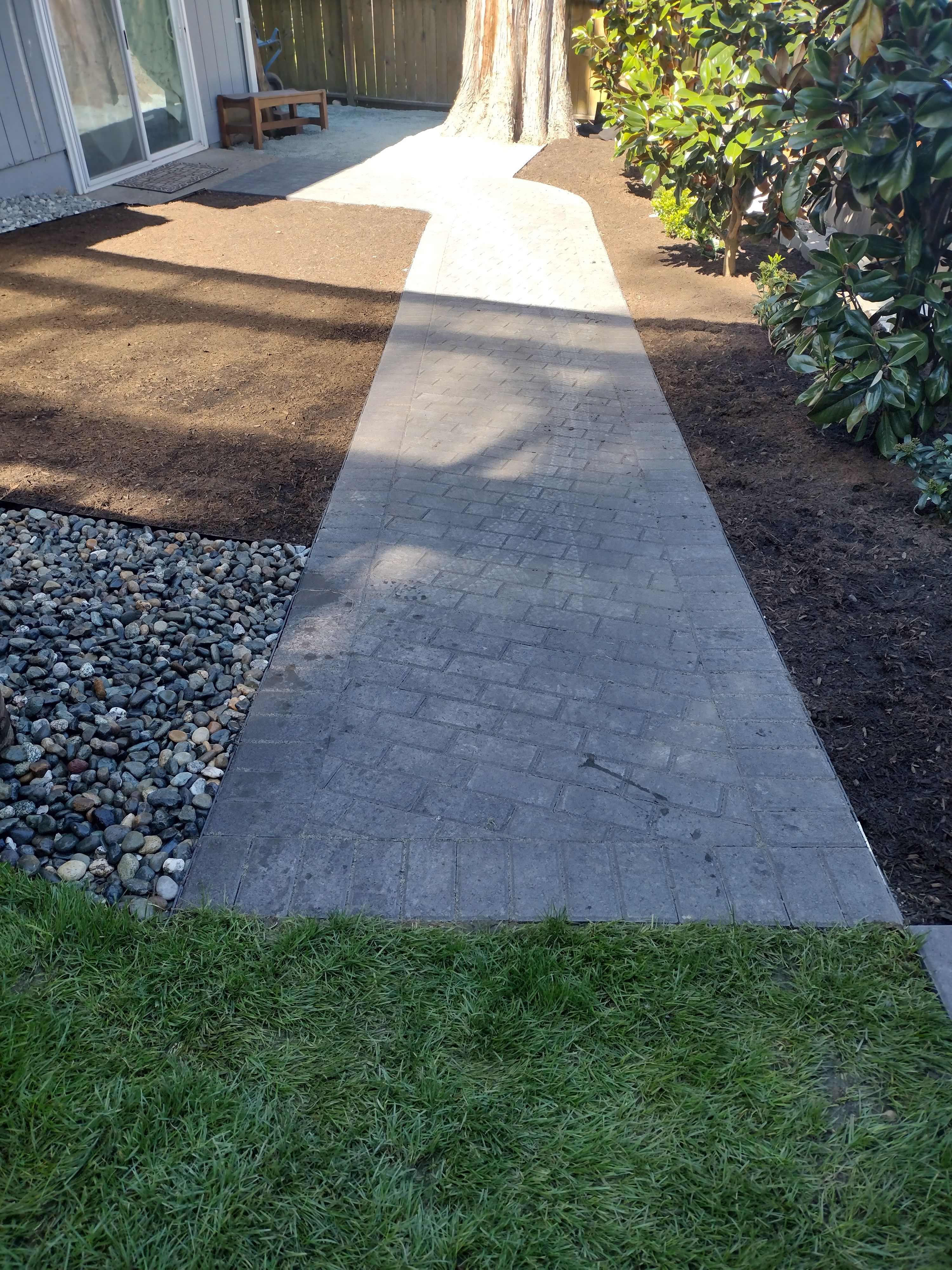 Brick-pattern walkway bordered by river rock and new lawn