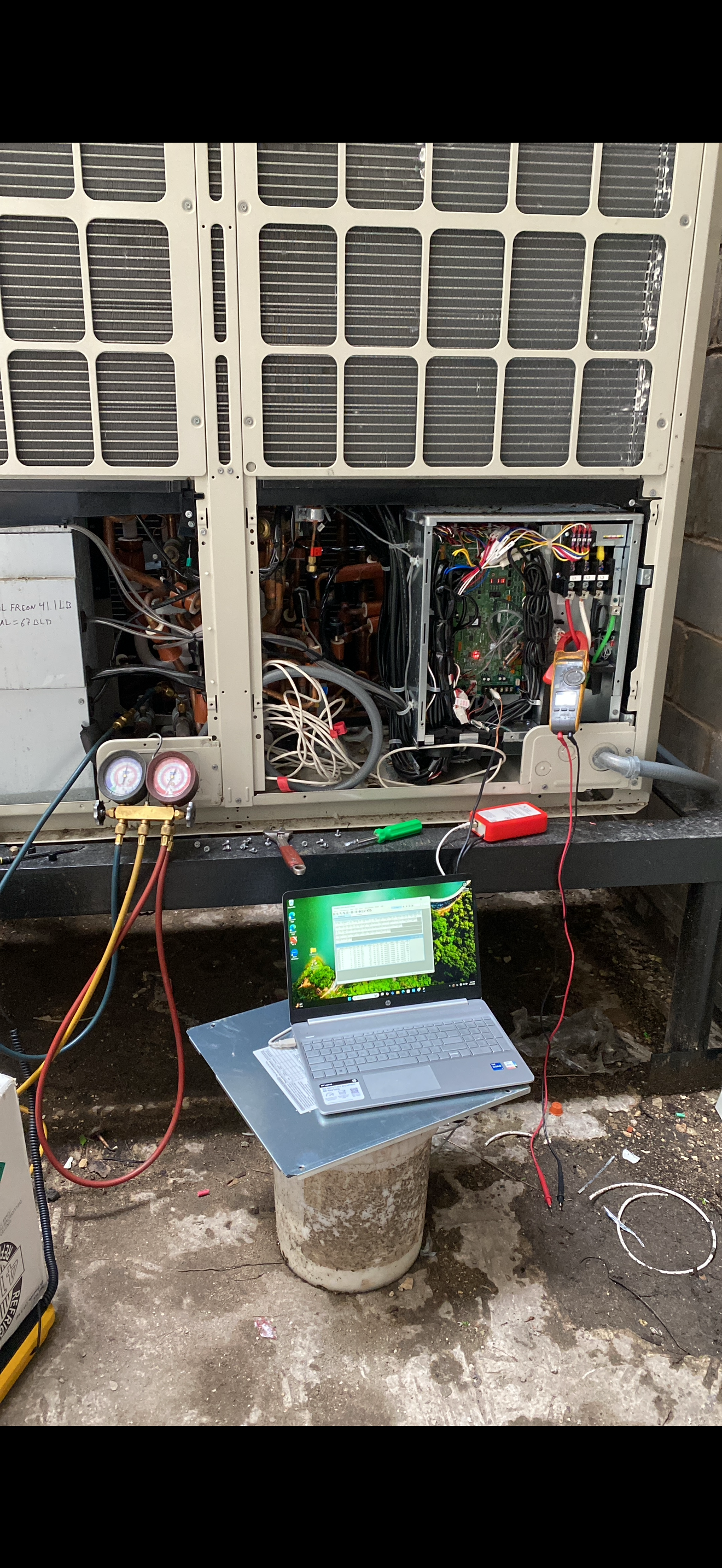 Refrigerant manifold gauges, a multimeter and a service laptop connected to an outdoor unit with its control panel open